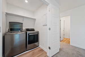 Laundry room featuring washing machine and clothes dryer, recessed lighting, electric panel, light wood-type flooring, and light carpet