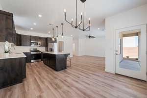 Kitchen with appliances with stainless steel finishes, dark brown cabinetry, light countertops, a kitchen bar, and light wood-type flooring