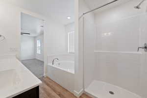 Bathroom with double vanity, a bath, walk in shower, and wood finished floors
