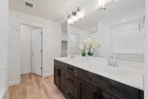 Full bathroom with double vanity, wood finished floors, a shower with shower door, and a walk in closet