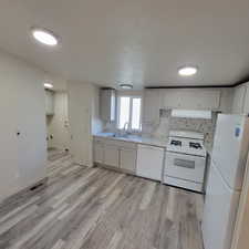 Kitchen featuring white appliances, decorative backsplash, light wood-type flooring, exhaust hood, and light stone countertops