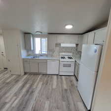 Kitchen featuring white appliances, backsplash, light wood-type flooring, and exhaust hood