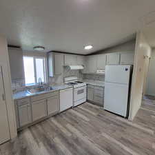 Kitchen featuring backsplash, white appliances, light wood finished floors, under cabinet range hood, and a textured ceiling