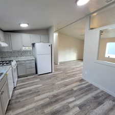 Kitchen with decorative backsplash, white appliances, light wood-style floors, light stone counters, and vaulted ceiling
