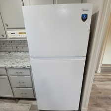 Kitchen view of gray cabinets, freestanding refrigerator, light wood-style flooring, light stone countertops, and tasteful backsplash