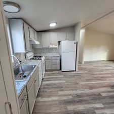 Kitchen featuring decorative backsplash, lofted ceiling, white appliances, light wood-style floors, and gray cabinetry