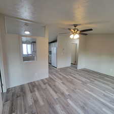 Unfurnished living room with a textured ceiling, light wood-style floors, and ceiling fan