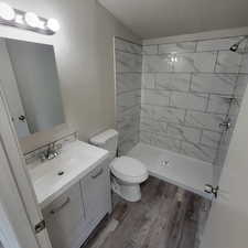 Full bathroom featuring vanity, wood finished floors, tiled shower, and a textured wall