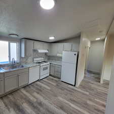 Kitchen featuring backsplash, white appliances, light wood-style floors, and under cabinet range hood