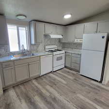 Kitchen with white appliances, decorative backsplash, light wood-style floors, and wall chimney exhaust hood
