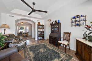 Living area featuring a ceiling fan, a textured ceiling, a tray ceiling, light wood-style flooring, and arched walkways