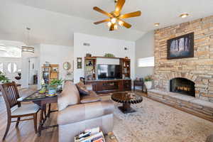 Living area with wood finished floors, ceiling fan, high vaulted ceiling, a stone fireplace, and a textured ceiling