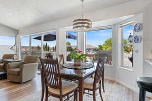 Dining area featuring a chandelier, light wood-style floors, a textured ceiling, and lofted ceiling