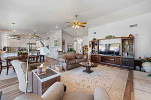Living room with ceiling fan, light wood-style flooring, a textured ceiling, and lofted ceiling