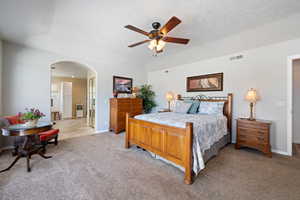 Bedroom with arched walkways, light colored carpet, a textured ceiling, and ceiling fan