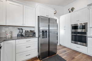 Kitchen featuring stainless steel appliances, white cabinetry, backsplash, stone countertops, and light wood-style flooring