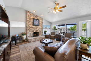 Living room with vaulted ceiling, light wood-type flooring, healthy amount of natural light, ceiling fan, and a textured ceiling