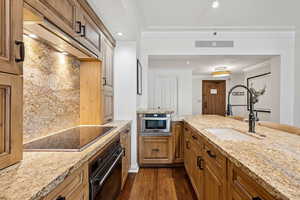 Kitchen featuring dark wood-style floors, black appliances, light stone countertops, decorative backsplash, and brown cabinetry