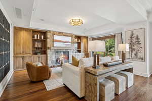Living room with crown molding, dark wood-style flooring, a stone fireplace, and built in features