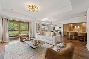 Living area with a tray ceiling, dark wood-style flooring, and ornamental molding