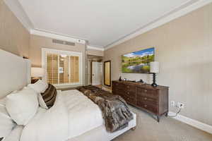 Bedroom with wallpapered walls, light carpet, and ornamental molding
