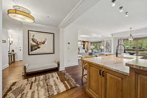Kitchen with dark wood-style floors, light stone counters, brown cabinets, ornamental molding, and a breakfast bar