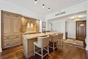 Kitchen featuring a breakfast bar, light stone countertops, backsplash, an island with sink, and dark wood-style floors