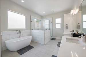 Bathroom featuring a stall shower, double vanity, a freestanding tub, healthy amount of natural light, and recessed lighting