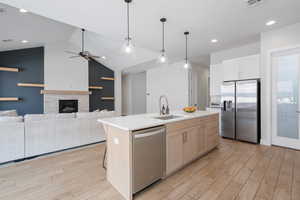 Kitchen with stainless steel appliances, light wood-type flooring, light countertops, decorative light fixtures, and lofted ceiling