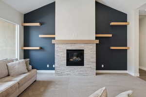 Living area featuring lofted ceiling, a stone fireplace, and carpet floors