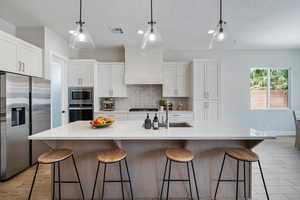 Kitchen with stainless steel appliances, decorative backsplash, white cabinetry, a breakfast bar, and a textured ceiling