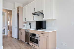 Kitchen featuring appliances with stainless steel finishes, under cabinet range hood, light countertops, light wood-style flooring, and white cabinets