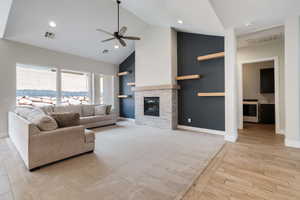 Living area with ceiling fan, a fireplace, light wood-style flooring, and high vaulted ceiling