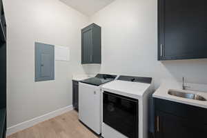 Laundry room with cabinet space, washing machine and clothes dryer, light wood-style flooring, and electric panel