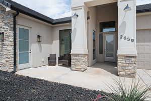 Doorway to property with stone siding, stucco siding, and a shingled roof