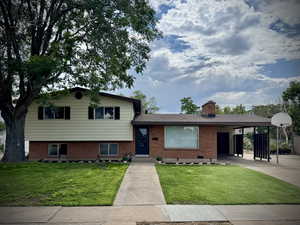 Tri-level home featuring brick siding, a front lawn, driveway, a chimney, and an attached carport