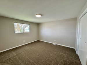Unfurnished room featuring dark carpet and baseboards