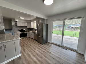 Kitchen featuring appliances with stainless steel finishes, decorative backsplash, gray cabinetry, light wood-style floors, and open shelves