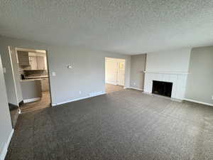 Unfurnished living room featuring a brick fireplace, carpet, and a textured ceiling