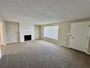Unfurnished living room with a textured ceiling, carpet flooring, and a brick fireplace