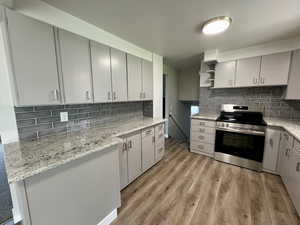 Kitchen featuring stainless steel range with electric stovetop, tasteful backsplash, light wood-style floors, gray cabinets, and open shelves