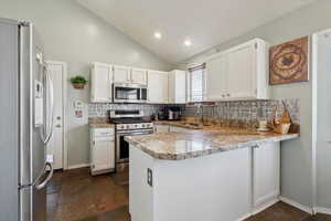 Kitchen with stainless steel appliances, tasteful backsplash, a peninsula, white cabinets, and lofted ceiling