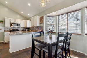 Dining area featuring plenty of natural light, recessed lighting, vaulted ceiling, a chandelier, and stone tile floors