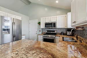 Kitchen featuring appliances with stainless steel finishes, light stone counters, tasteful backsplash, white cabinets, and beam ceiling