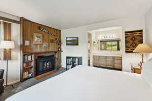 Carpeted bedroom featuring a fireplace with flush hearth, wood walls, and ensuite bathroom