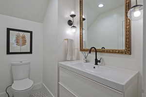 Half bathroom featuring vanity, vaulted ceiling, tile patterned floors, and recessed lighting