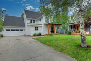 View of front facade featuring roof with shingles, a front yard, concrete driveway, an attached garage, and a porch