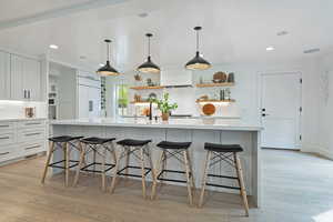 Kitchen with open shelves, light wood-style floors, white cabinets, light countertops, and a breakfast bar