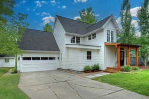 View of front facade featuring roof with shingles, concrete driveway, board and batten siding, and a front yard