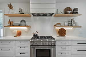 Kitchen with open shelves, stainless steel stove, extractor fan, white cabinets, and light countertops